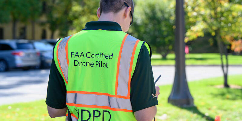 A man in an NDPD FAA certified drone pilot safety vest seen from the back