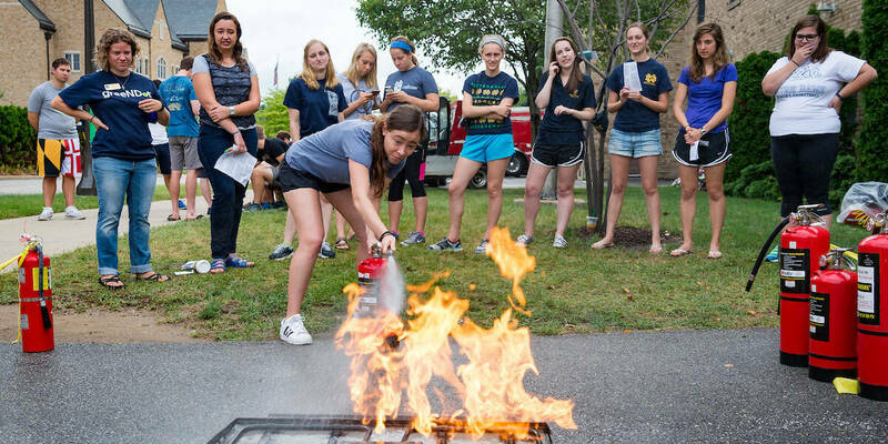 A woman uses a fire extinguisher as others look on during fire safety training