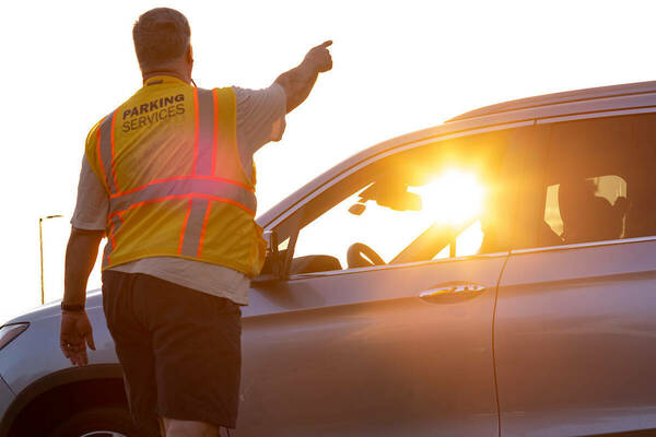 Man in parking services safety vest points a motorist where they should go