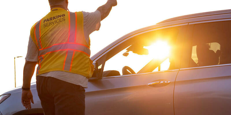 Man in parking services safety vest points a motorist where they should go